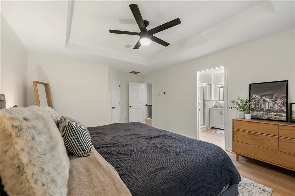 Bedroom featuring ensuite bath, a raised ceiling, ceiling fan, and light wood-type flooring