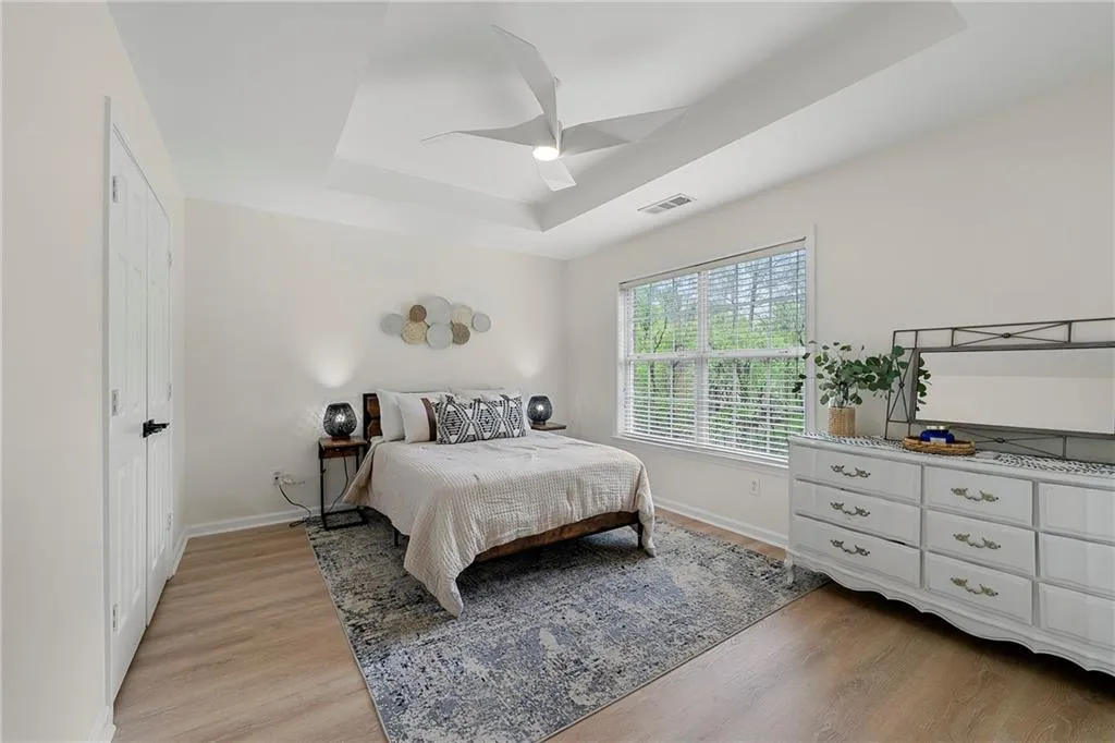 Bedroom with light hardwood / wood-style flooring, ceiling fan, and a raised ceiling
