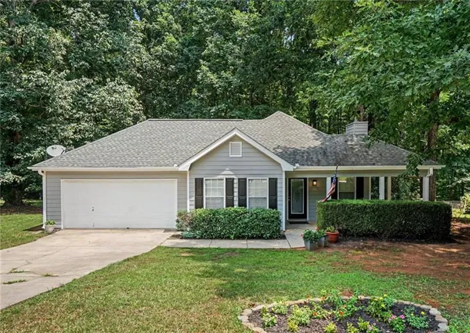 Gray siding exterior with dark shutters, an attached garage, a covered front porch, and a landscaped front yard with mature trees