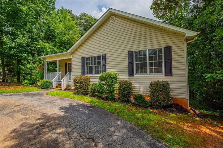 Siding exterior with a covered front porch featuring white railings, surrounded by mature trees and landscaping