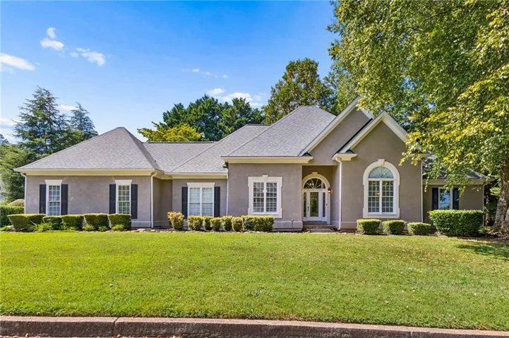 Stucco exterior with a gabled roofline, arched entry, decorative window shutters, and manicured landscaping