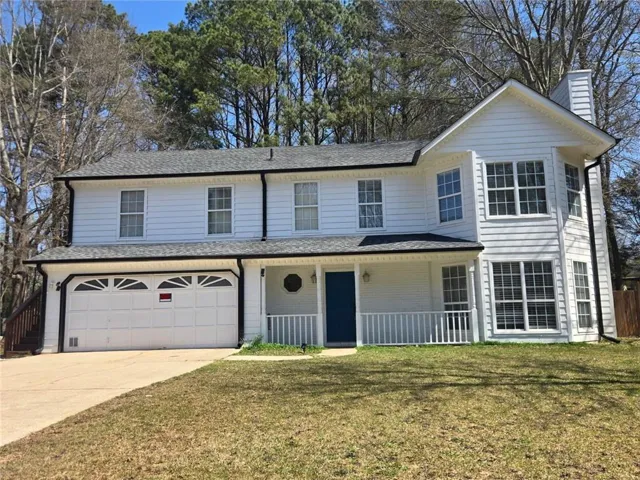 Two-story residence featuring white siding, a covered porch with white railings, a blue entry door, and a two-car garage with decorative window inserts