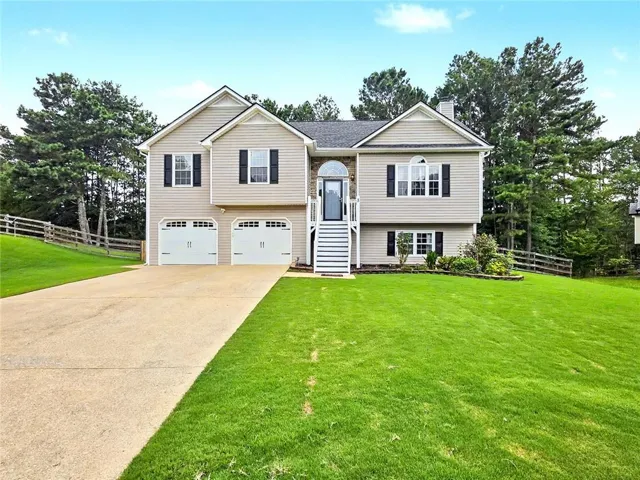 Two-car garage with white paneled doors, expansive driveway, and a split-level entry