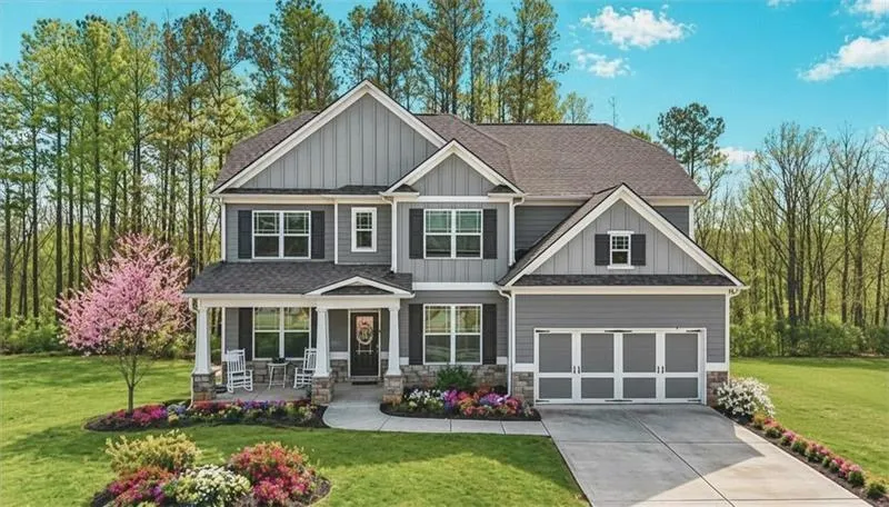 Two-story gray siding residence featuring a covered front porch, stone accents, a two-car garage, manicured landscaping, and a paved driveway