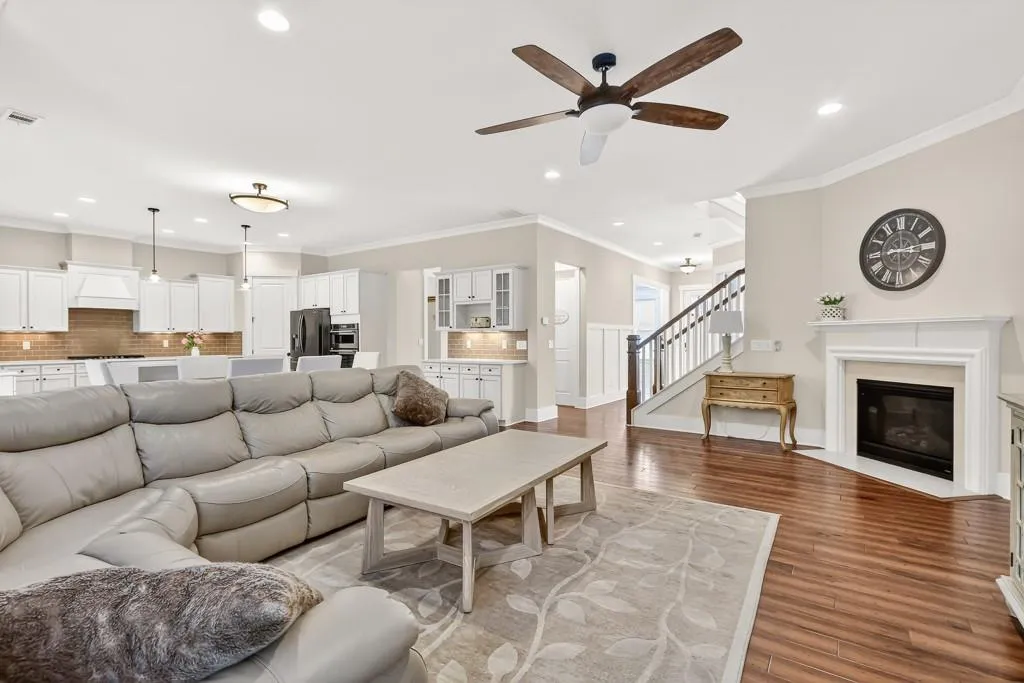 Living room featuring wood finished floors, crown molding, a ceiling fan, a high end fireplace, and recessed lighting