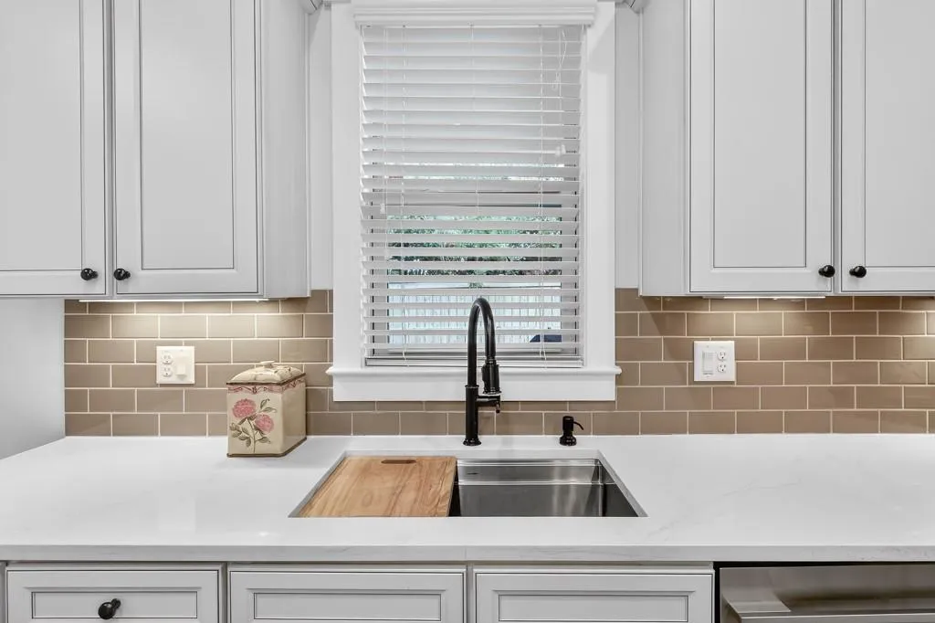 Kitchen with light stone countertops, white cabinets, and backsplash