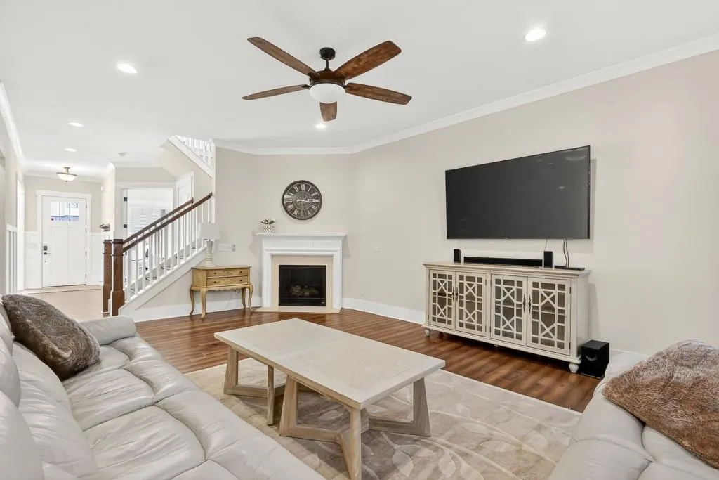 Living area with crown molding, wood finished floors, ceiling fan, recessed lighting, and a fireplace with flush hearth