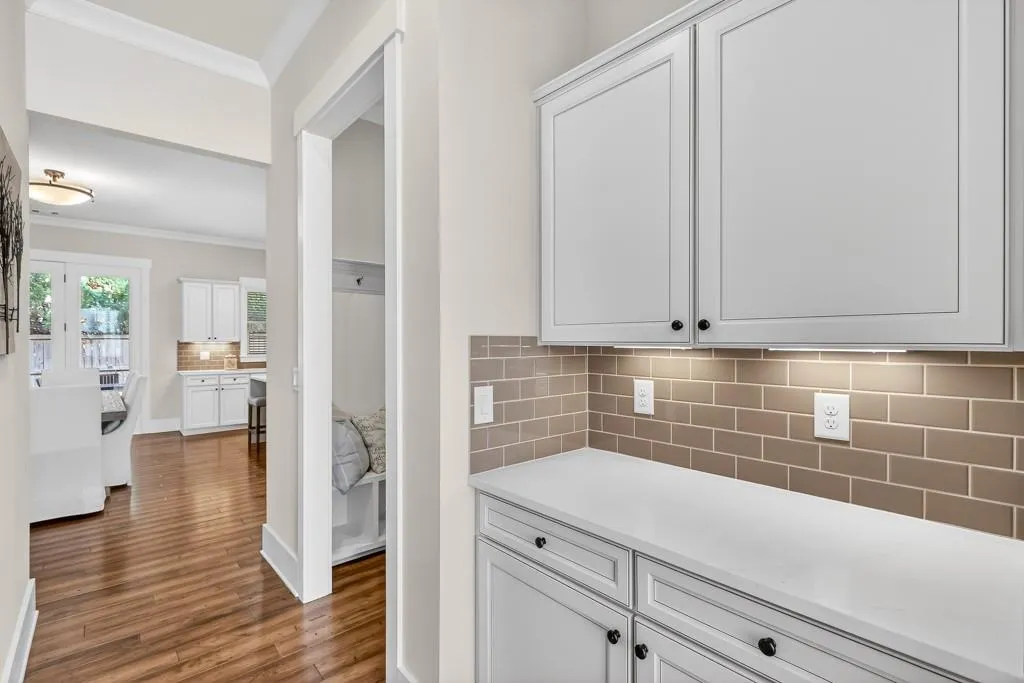 Bar featuring tasteful backsplash, crown molding, white cabinetry, light stone counters, and dark wood-type flooring