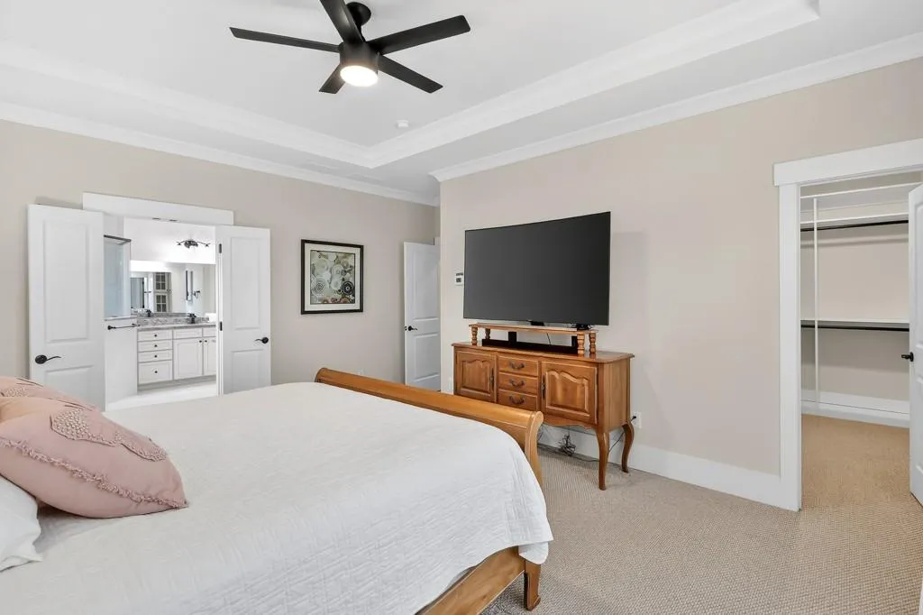 Bedroom featuring crown molding, light colored carpet, a walk in closet, a raised ceiling, and a ceiling fan