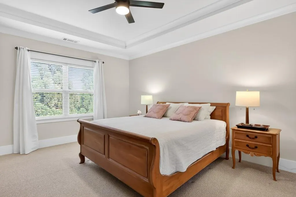 Bedroom with light colored carpet, a ceiling fan, crown molding, and a raised ceiling
