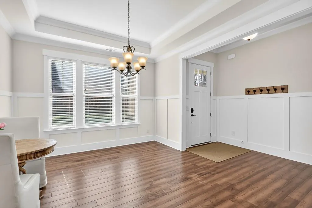 Unfurnished dining area with a decorative wall, a wainscoted wall, dark wood-type flooring, hanging lights, and a raised ceiling