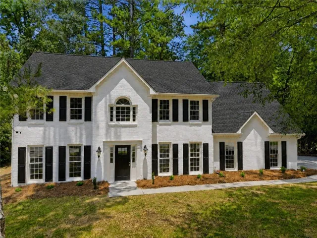 Two-story residence featuring a white brick exterior, black shutters, and a dark shingle roof