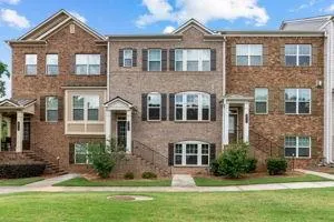 Multi-story townhome exterior featuring a brick facade with stone accents, multiple window styles including arched and rectangular, decorative shutters, and individual covered entryways