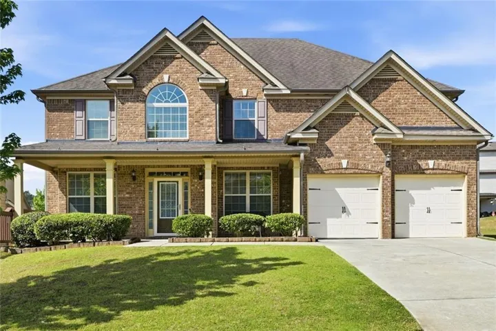 Brick facade with a covered front porch featuring columns, arched window, two-car garage, and a concrete driveway
