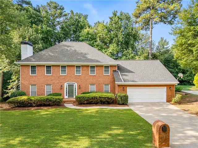 Brick-front residence featuring a two-car garage, mature landscaping, and an arched entry