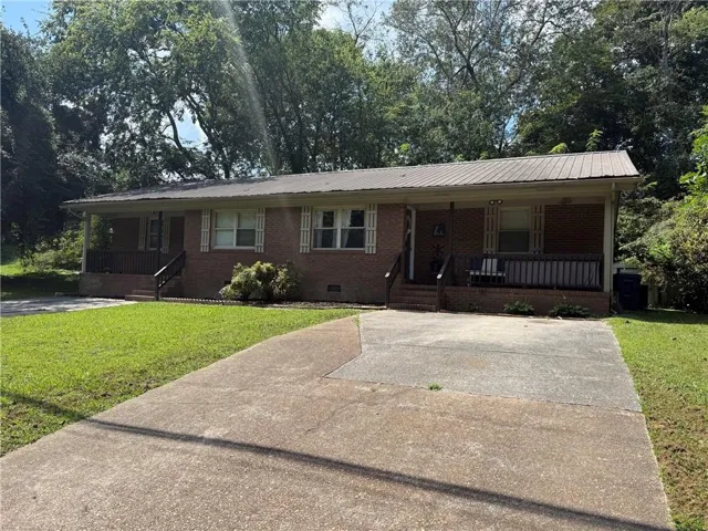 Brick exterior featuring a metal roof, twin covered porches, and a concrete driveway