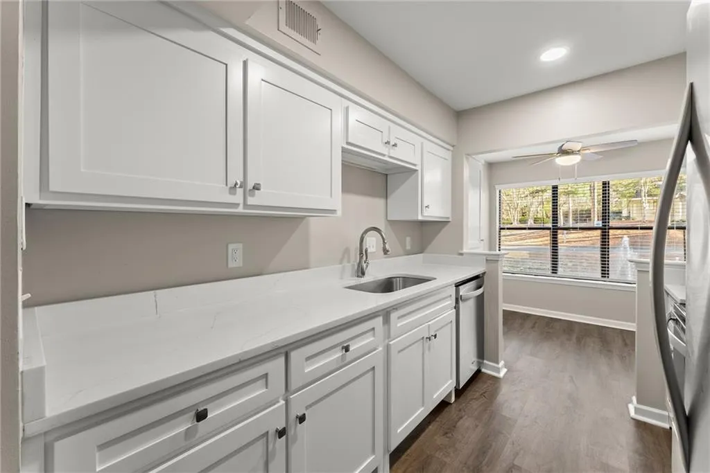 Kitchen with stainless steel dishwasher, white cabinets, sink, and light stone counters