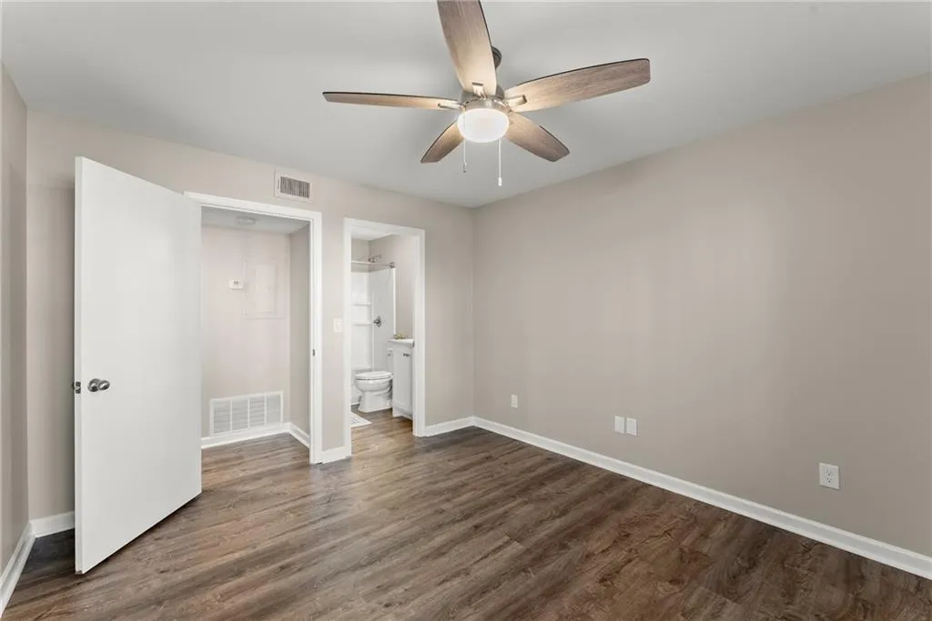 Unfurnished bedroom featuring ceiling fan, connected bathroom, and dark hardwood / wood-style floors