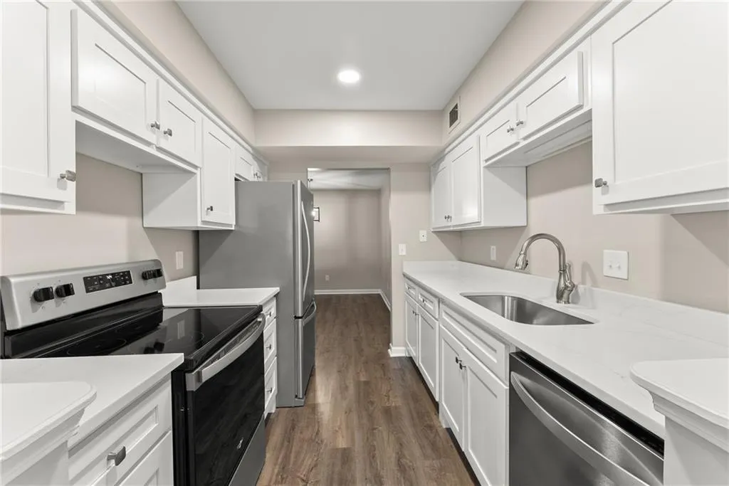 Kitchen with light stone countertops, white cabinetry, stainless steel appliances, sink, and dark hardwood / wood-style floors