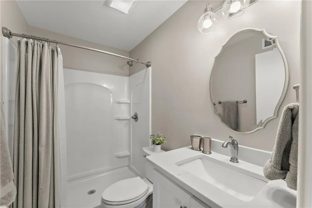 Bathroom with toilet, vanity, and curtained shower
