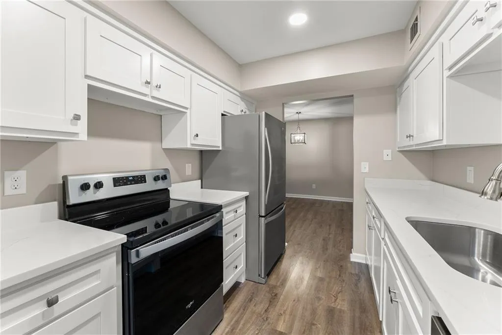 Kitchen with hardwood / wood-style floors, appliances with stainless steel finishes, white cabinetry, and sink