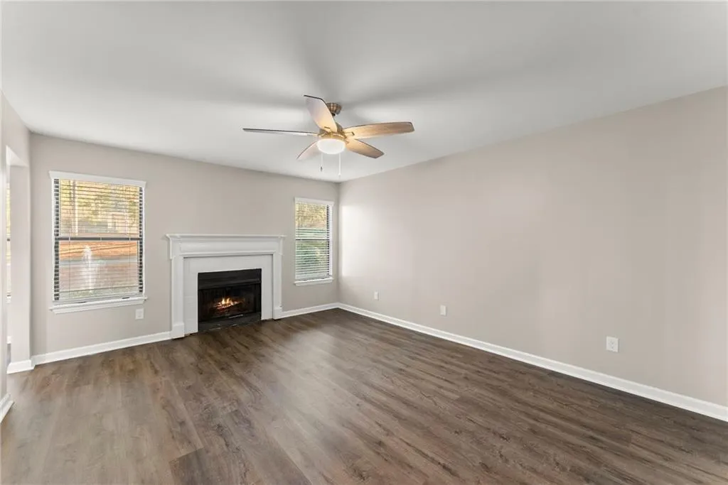 Unfurnished living room with dark wood-type flooring, a healthy amount of sunlight, and ceiling fan