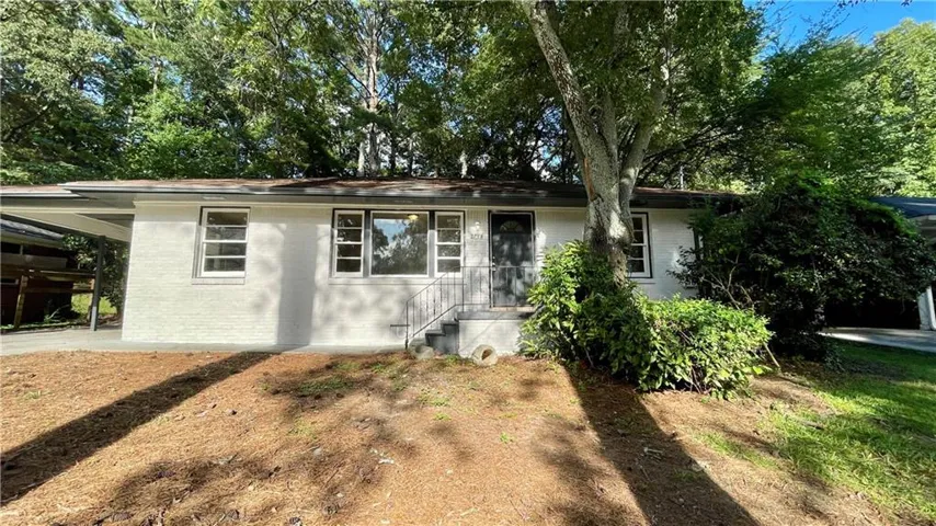 White brick exterior featuring a covered carport, multiple windows, and mature trees