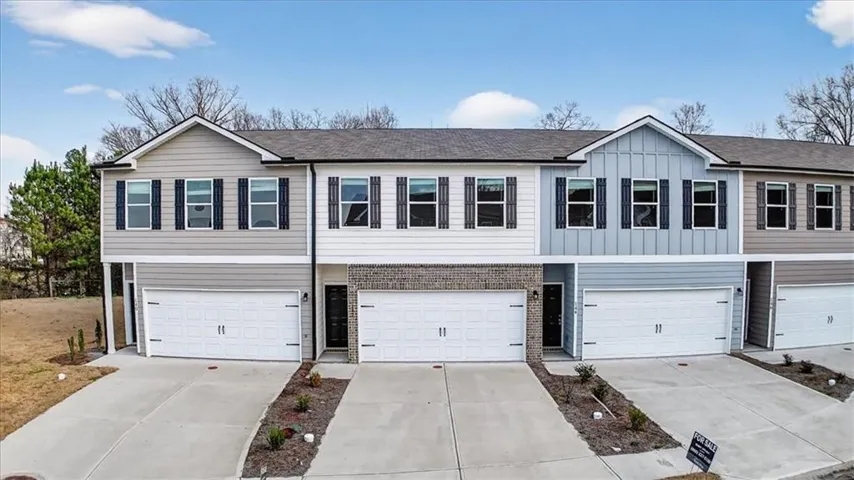 Multi-story townhome featuring varied siding textures, attached garages, and individual driveways