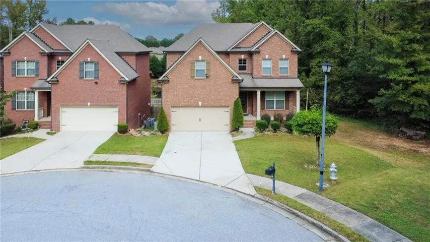 Traditional-style house featuring driveway, covered porch, brick siding, a front yard, and an attached garage