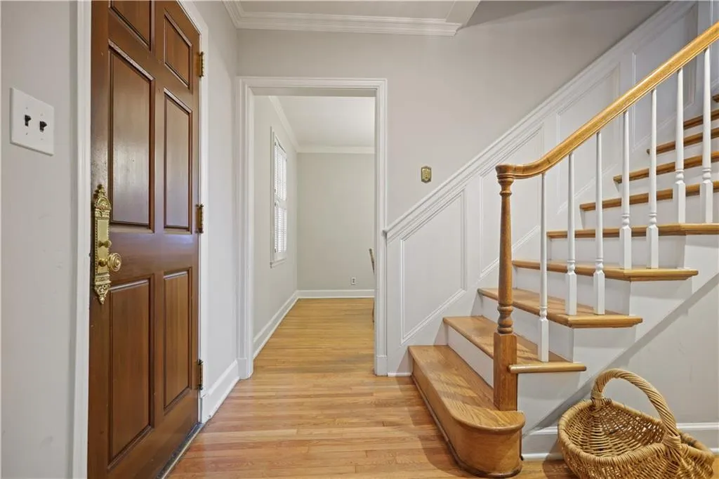 Entryway featuring a wood-panel door with brass hardware, wood-finish flooring, and a staircase with a wooden handrail and white balusters