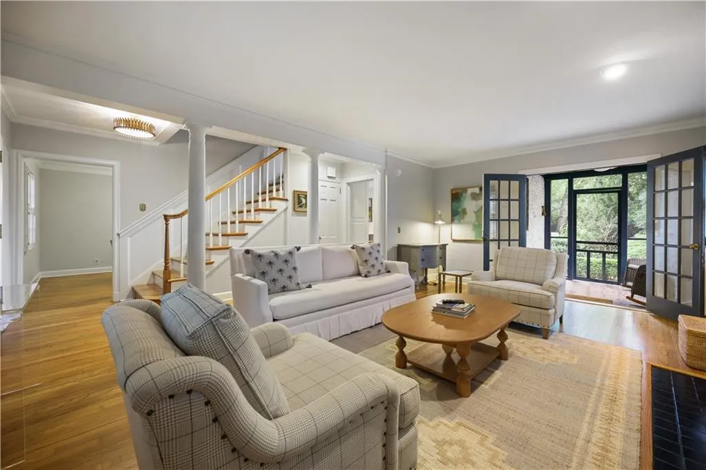 Hardwood flooring, architectural columns, staircase with wooden handrail, and multi-pane glass french doors