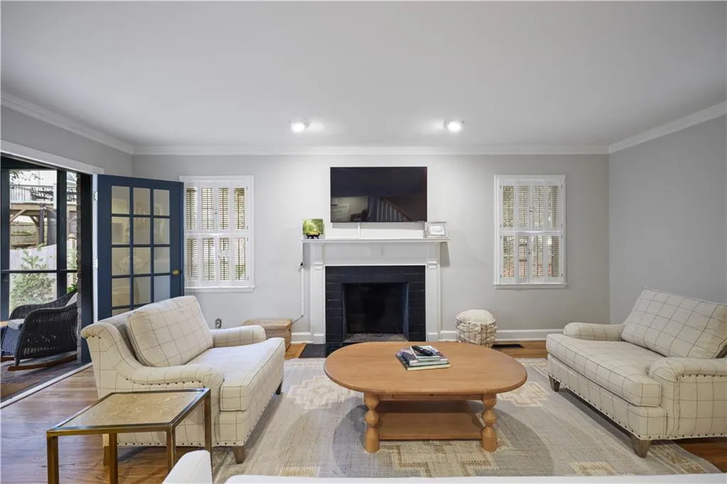 Living area featuring a fireplace with a dark surround and white mantel, wood-finish flooring, recessed lighting, and double-paned windows with interior shutters