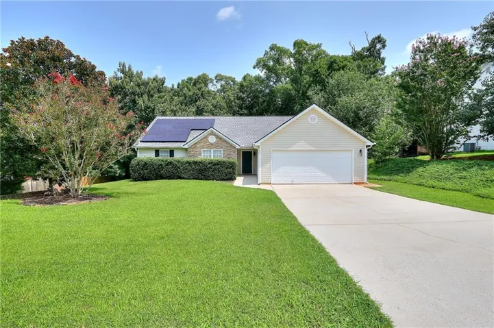 Exterior featuring stone accents, vinyl siding, a gray shingle roof with integrated solar panels, and a concrete driveway