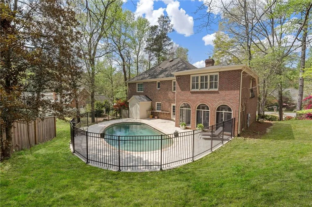Rear view of house featuring a patio, a chimney, brick siding, a fenced backyard, and a storage unit
