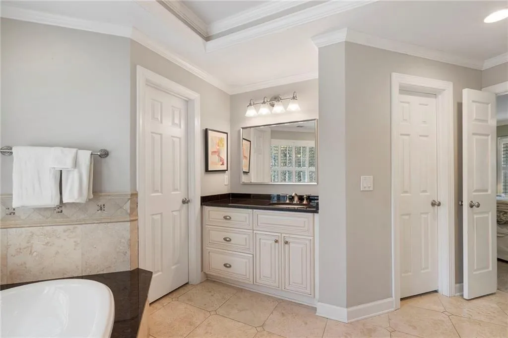 Ensuite bathroom featuring vanity, ornamental molding, light tile patterned floors, tile walls, and a garden tub