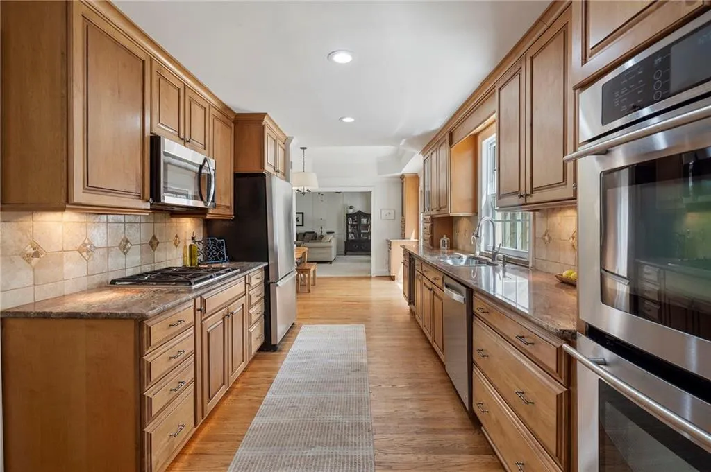Kitchen featuring stainless steel appliances, dark stone counters, wood finish cabinetry, light wood-style floors, and decorative backsplash