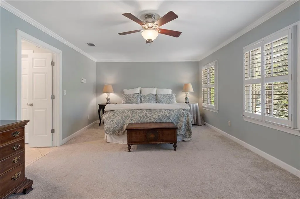 Bedroom with light carpet, crown molding, and a ceiling fan