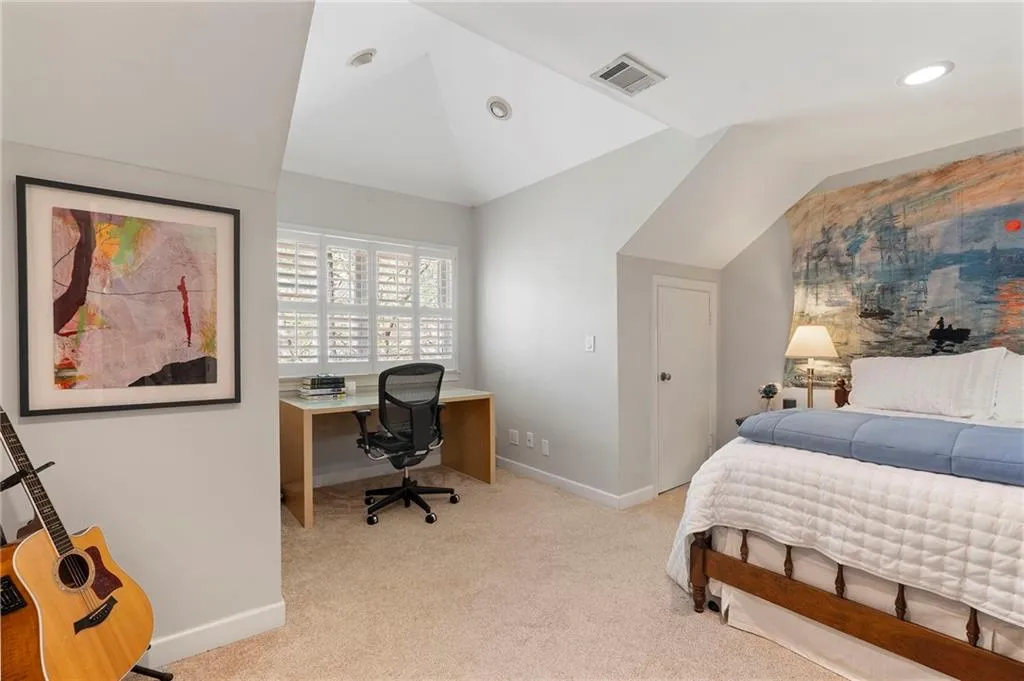 Bedroom with a desk, light colored carpet, and vaulted ceiling