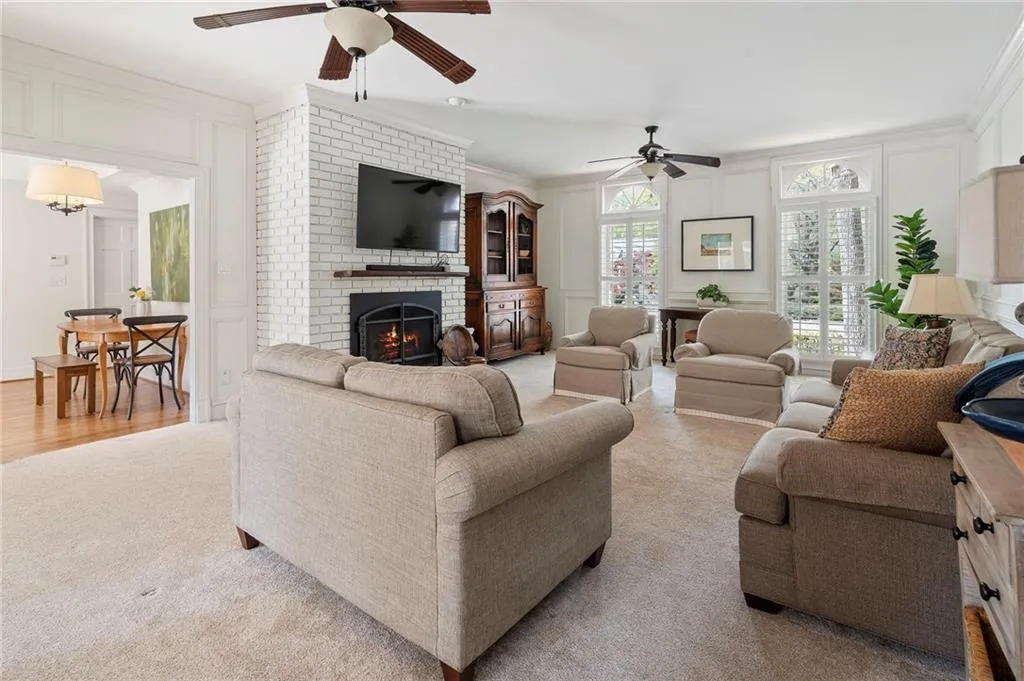 Living area with a decorative wall, ceiling fan, a fireplace, light colored carpet, and ornamental molding