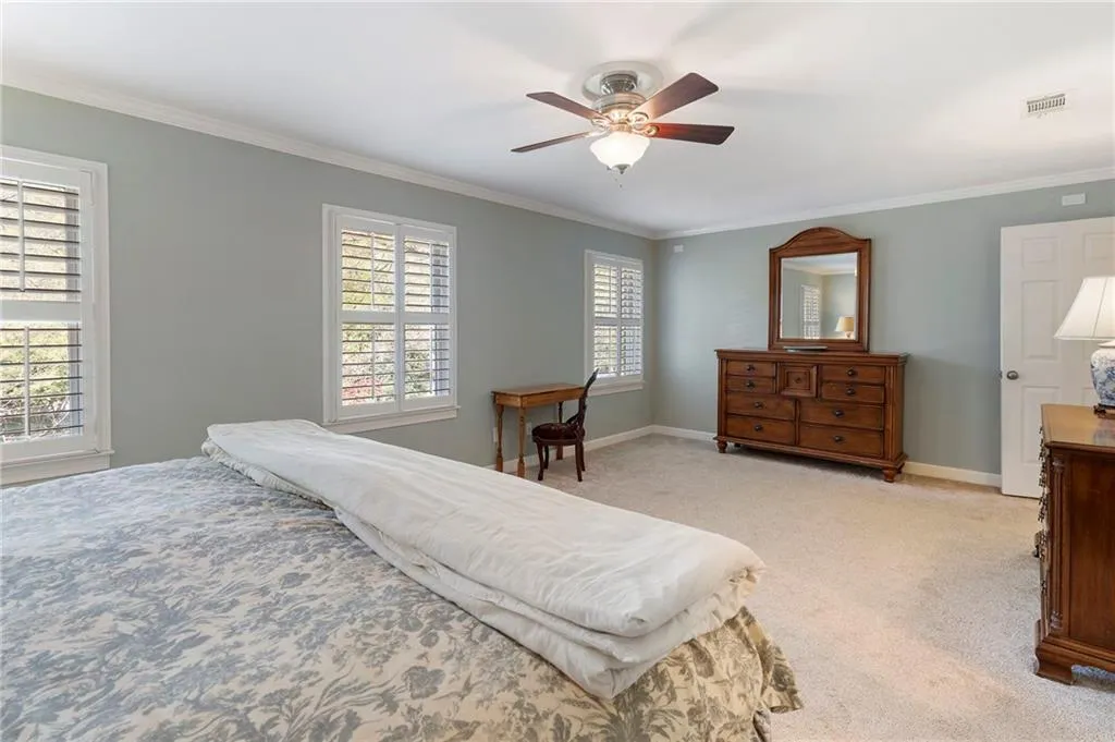 Bedroom with light carpet, ornamental molding, and a ceiling fan