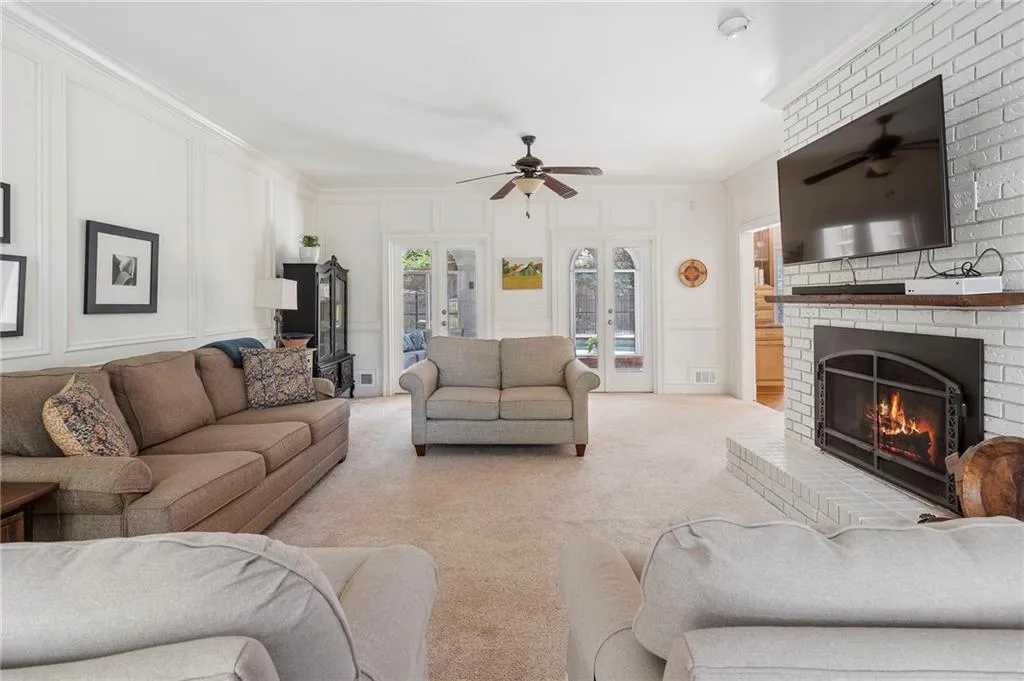 Living room with a decorative wall, a ceiling fan, a fireplace, carpet, and ornamental molding
