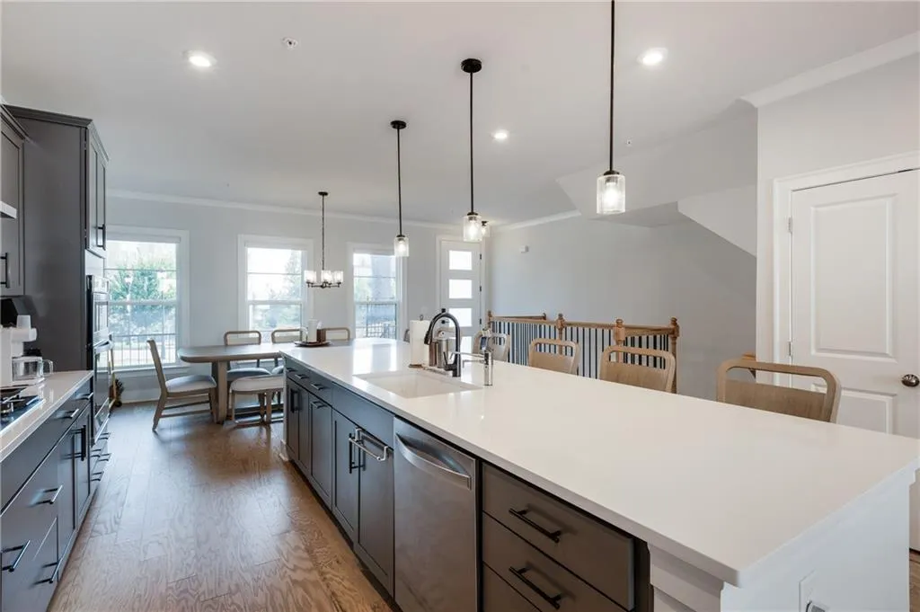 Kitchen with ornamental molding, pendant lighting, stainless steel dishwasher, light wood finished floors, and a center island with sink