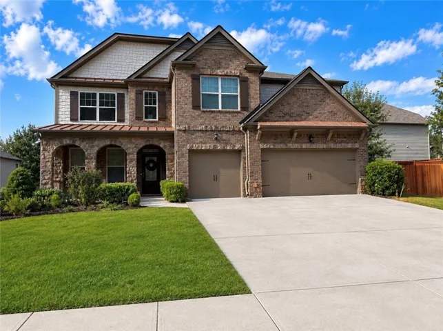 Brick and stone facade, covered entry porch with archways, two-car garage, concrete driveway, and established front landscaping