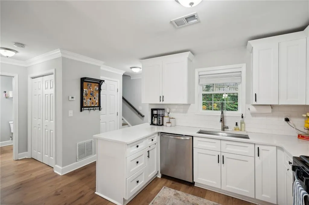 Kitchen with appliances with stainless steel finishes, sink, backsplash, white cabinetry, and wood-type flooring