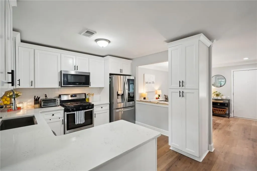 Kitchen featuring white cabinets, backsplash, light wood-type flooring, stainless steel appliances, and kitchen peninsula