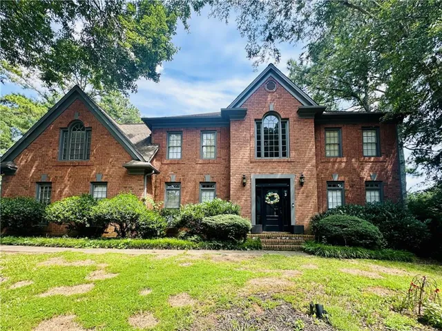 Brick exterior residence featuring a prominent gabled entry, arched window, dark-framed windows, and mature perimeter trees