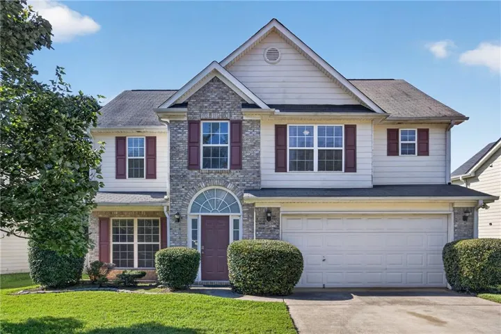 Two-story residence featuring a brick and siding exterior, two-car garage, arched entry with transom window, and red shutters
