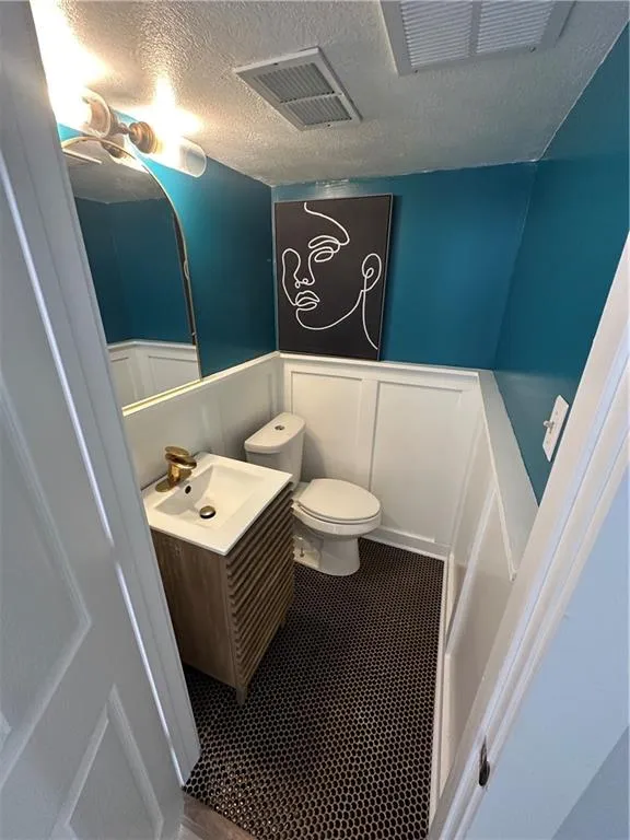 Half bathroom with vanity, a textured ceiling, a wainscoted wall, a decorative wall, and tile patterned floors