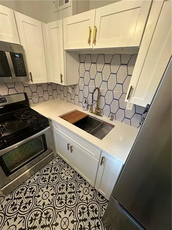 Kitchen featuring appliances with stainless steel finishes, decorative backsplash, white cabinetry, light stone counters, and tile patterned flooring