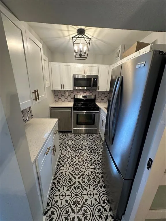 Kitchen featuring refrigerator, decorative backsplash, white cabinetry, and stainless steel gas stove